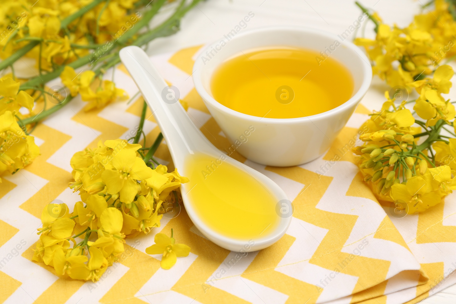 Photo of Rapeseed oil in gravy boat, bowl and beautiful yellow flowers on table