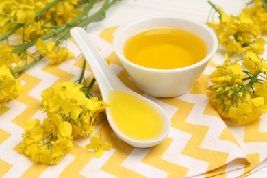 Rapeseed oil in gravy boat, bowl and beautiful yellow flowers on table