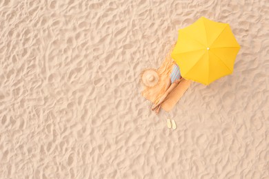 Woman resting under yellow beach umbrella at sandy coast, aerial view. Space for text