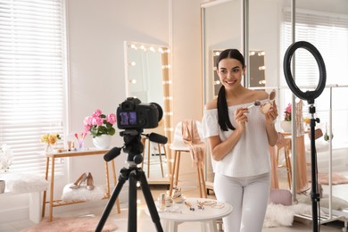 Photo of Blogger with makeup product recording video in dressing room at home. Using ring lamp and camera