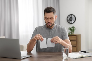 Photo of Man ripping photo at table indoors. Divorce concept