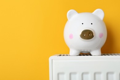 Photo of Piggy bank on heating radiator against orange background, space for text