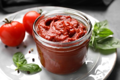 Photo of Jar of tasty tomato paste and ingredients on table, closeup