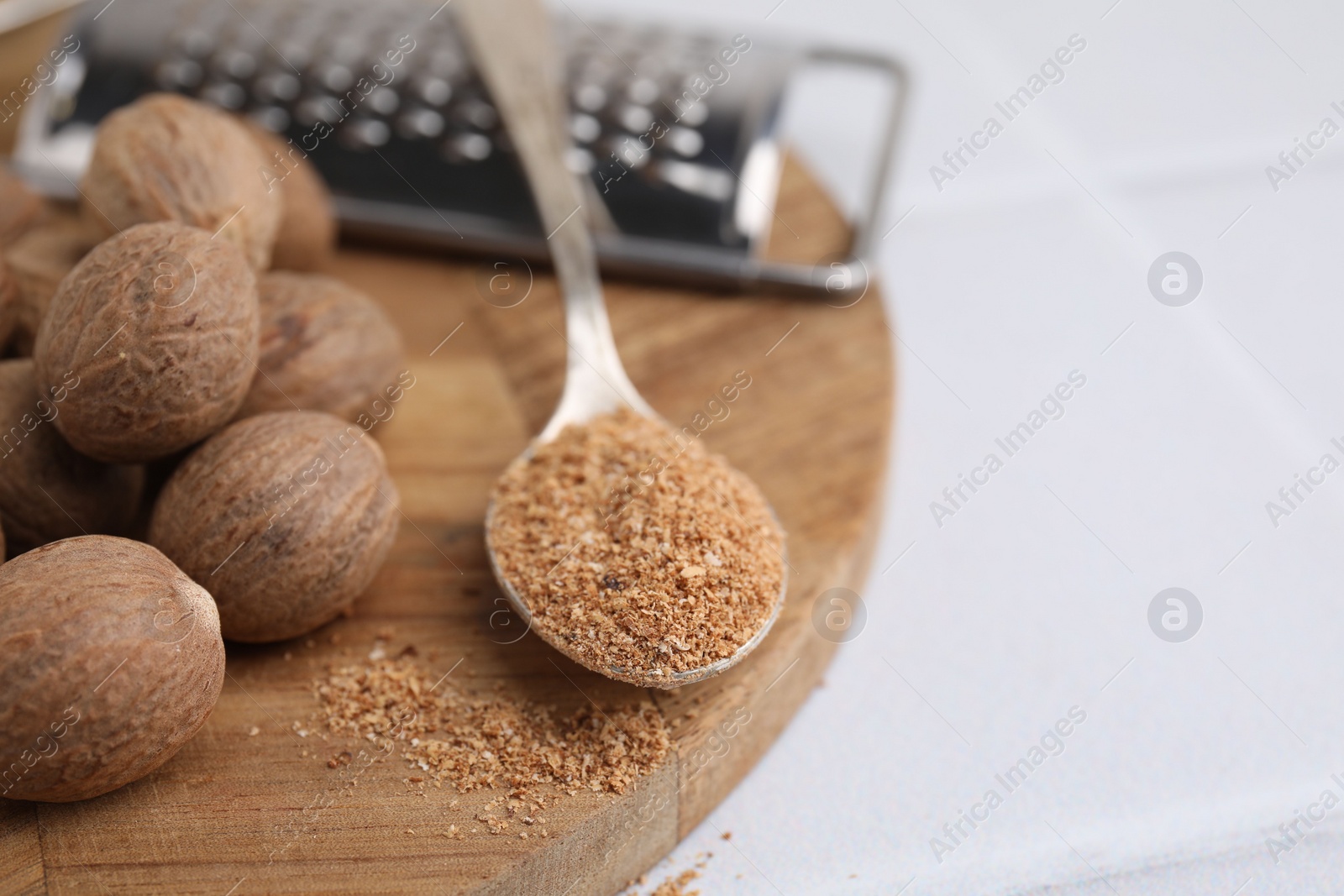 Photo of Spoon with grated nutmeg, seeds and grater on white table, closeup. Space for text