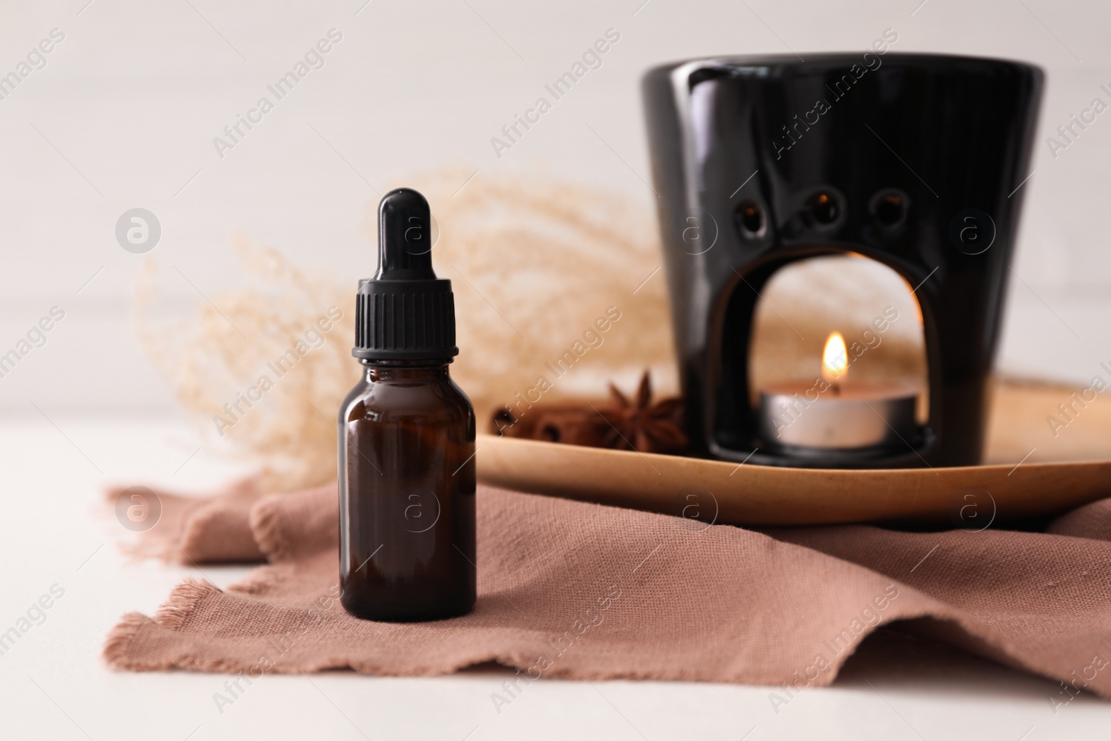 Photo of Aroma lamp and cinnamon essential oil on white table, space for text