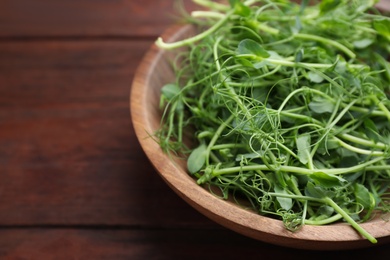 Photo of Plate with fresh microgreen on brown wooden table, closeup