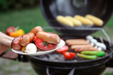 Photo of Woman holding plate with grilled food outdoors, closeup. Summer barbecue