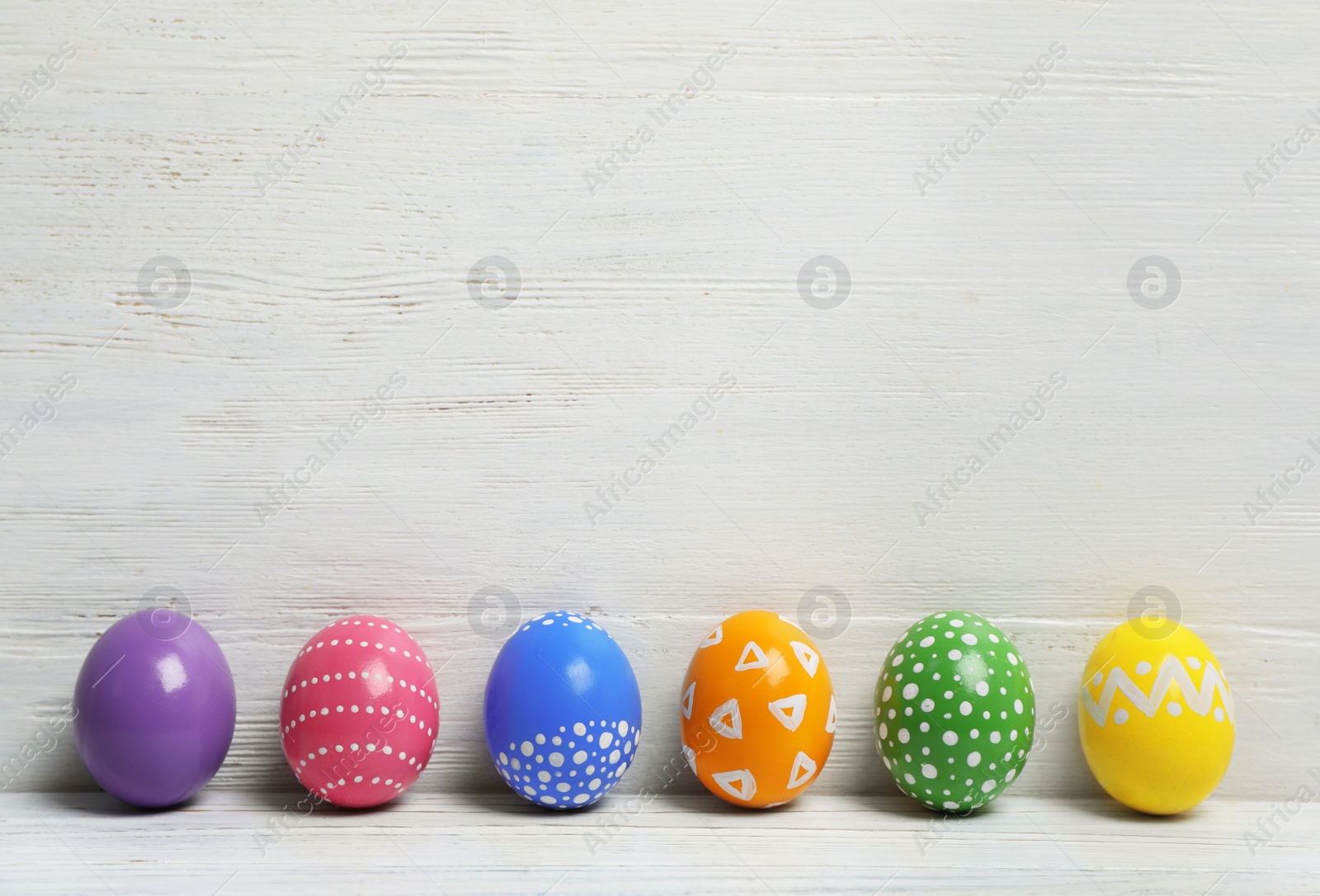 Photo of Decorated Easter eggs on table near wooden wall. Space for text