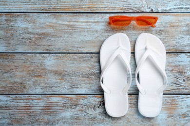 Stylish flip flops and sunglasses on light wooden background, flat lay. Space for text