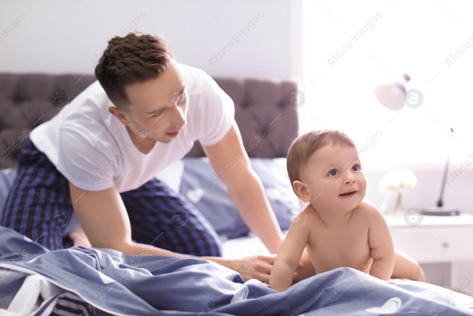 Photo of Young father with his cute little son on bed