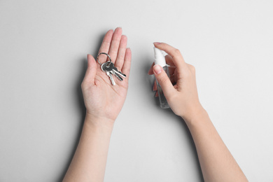 Photo of Woman spraying antiseptic onto keys on light grey background, top view