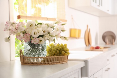 Photo of Bouquet of beautiful eustoma flowers and grapes on white table in kitchen. Interior design