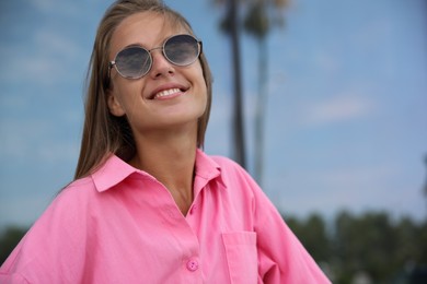 Portrait of beautiful young woman in stylish sunglasses near building outdoors, space for text