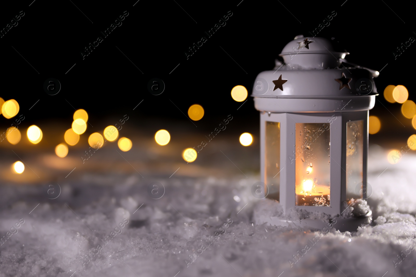 Photo of Lantern with burning candle and Christmas lights on white snow outdoors. Space for text