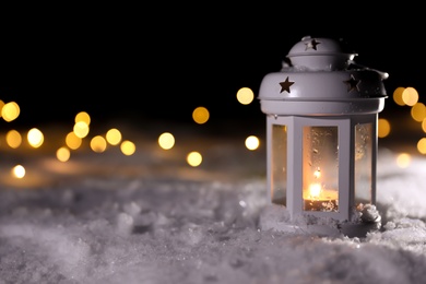 Photo of Lantern with burning candle and Christmas lights on white snow outdoors. Space for text