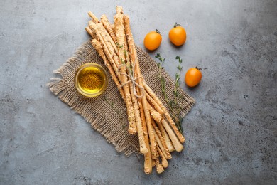 Photo of Delicious grissini sticks, oil, thyme and yellow tomatoes on grey table, flat lay