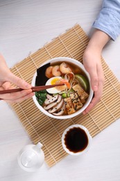 Photo of Woman eating delicious ramen with chopsticks at white table, top view. Noodle soup