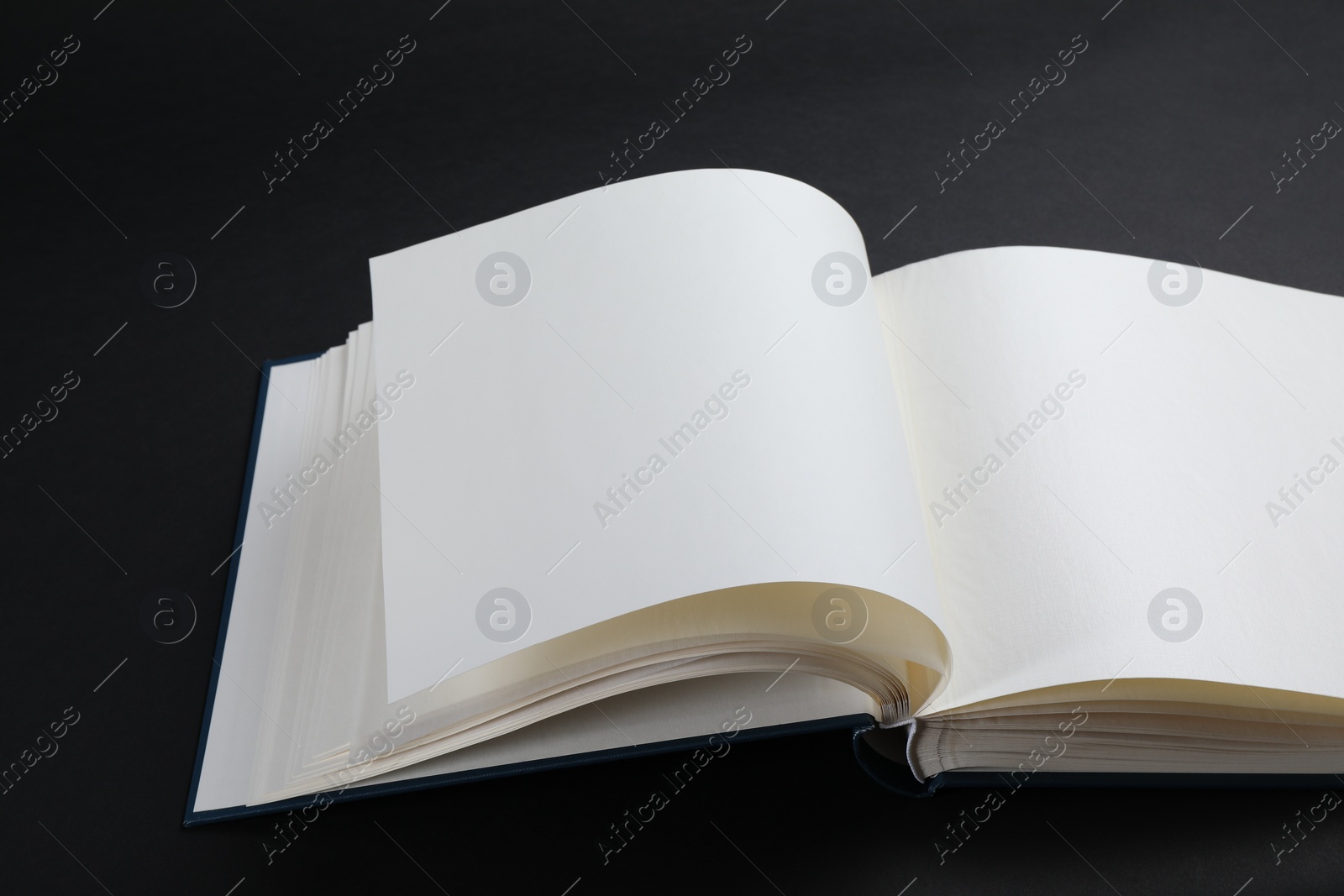 Photo of One open photo album on black background, closeup. Space for text