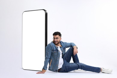 Image of Man sitting near huge mobile phone with empty screen on white background. Mockup for design