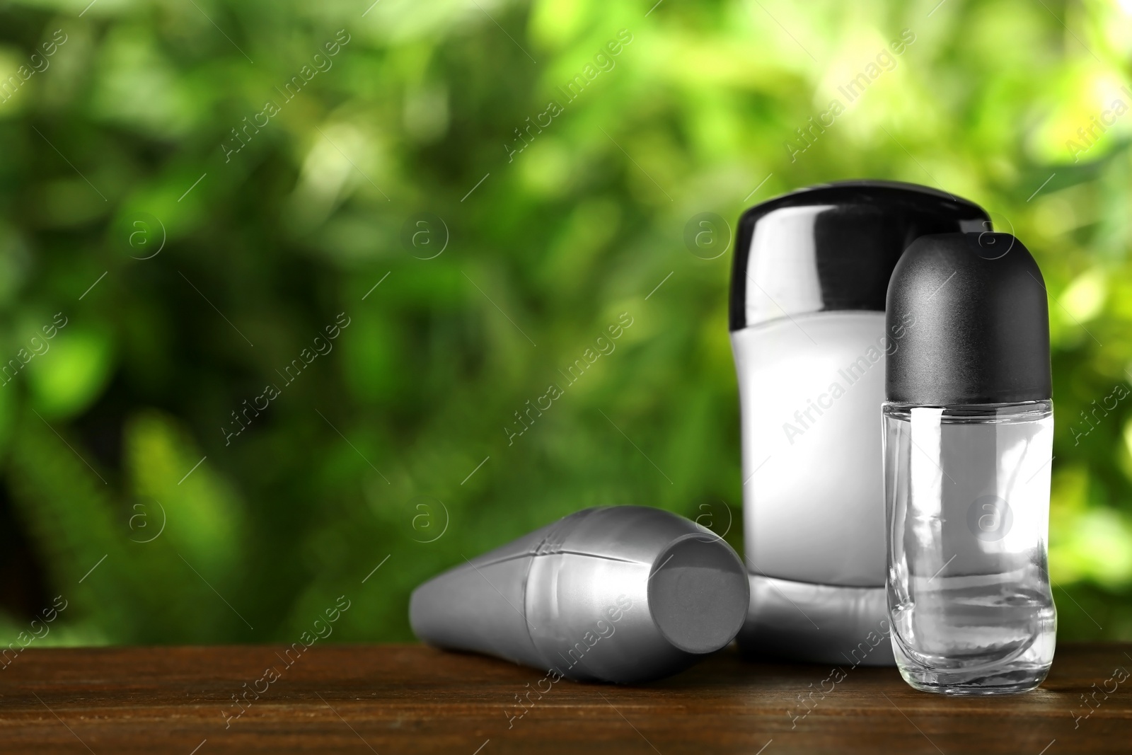 Photo of Set of different deodorants on wooden table against blurred green background. Space for text