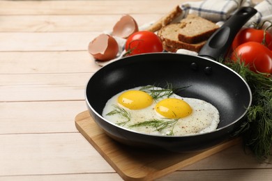 Photo of Frying pan with tasty cooked eggs, dill and other products on light wooden table. Space for text
