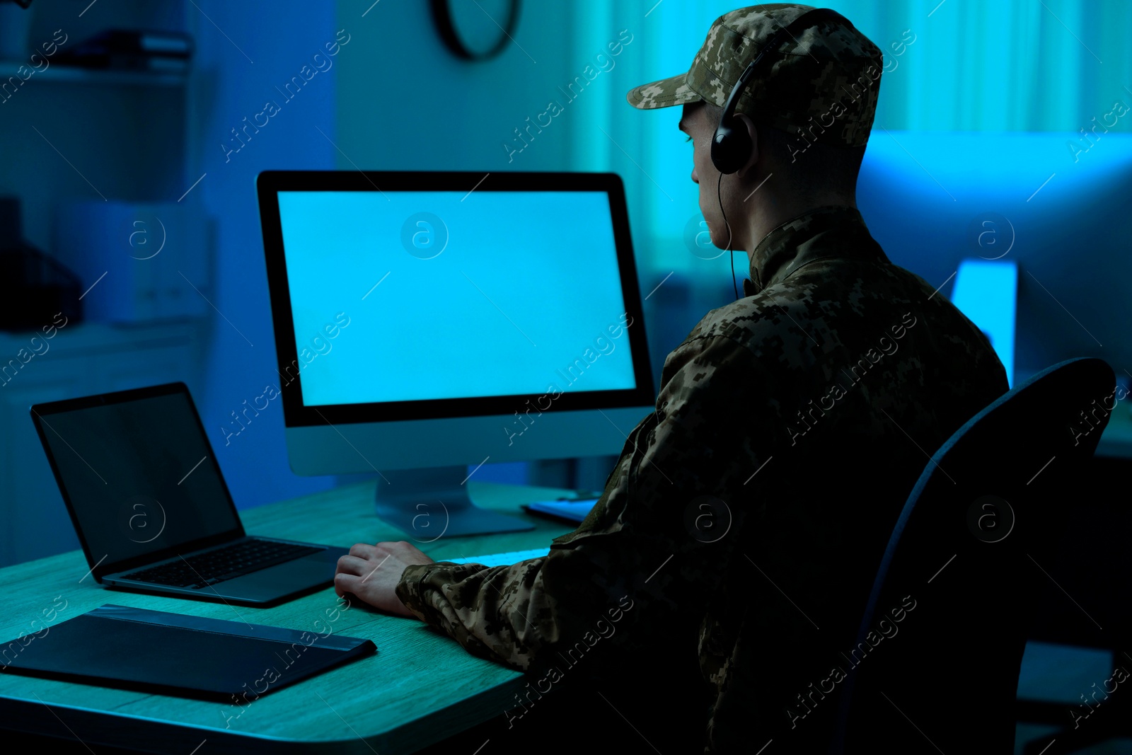 Image of Military service. Soldier in headphones working at wooden table in office at night