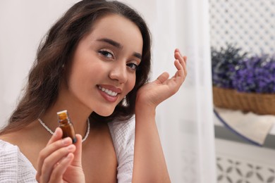 Photo of Beautiful happy woman with bottle of essential oil indoors