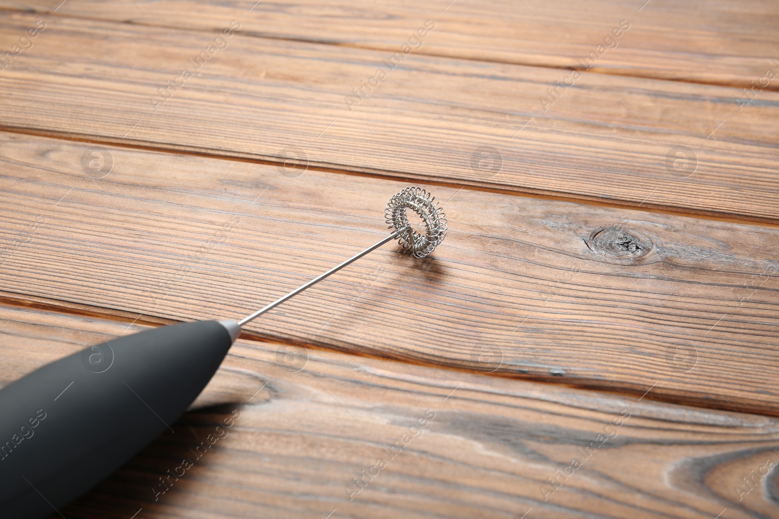 Photo of Black milk frother wand on wooden table, closeup. Space for text