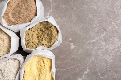 Photo of Bags with different types of flour on grey background, top view. Space for text