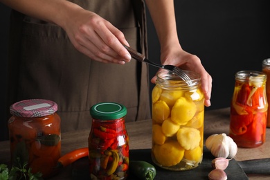 Photo of Woman taking pickled pattypan squash from jar at wooden table, closeup