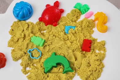 Photo of Bright kinetic sand and toys on white table, flat lay