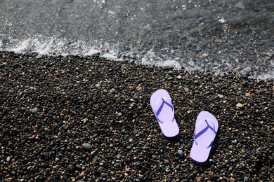 Photo of Stylish lilac flip lops on pebble beach near sea, above view. Space for text