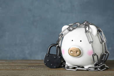 Photo of Piggy bank with steel chain, padlock on wooden table, space for text. Money safety concept