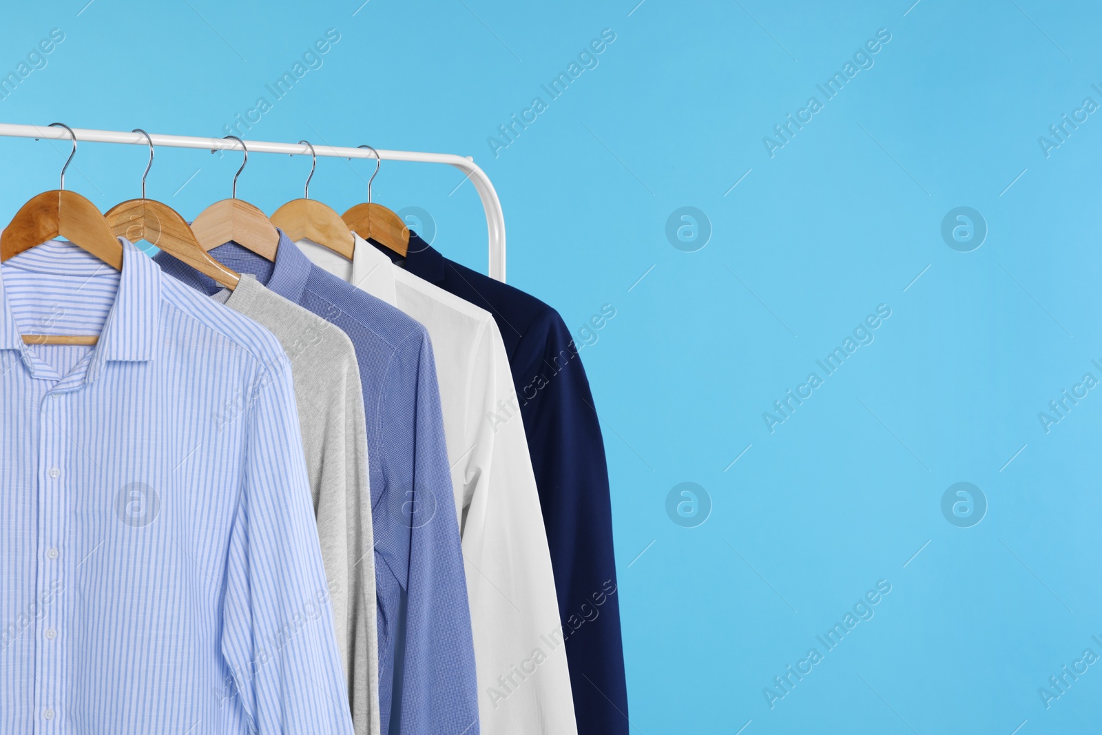 Photo of Rack with stylish clothes on wooden hangers against light blue background, space for text