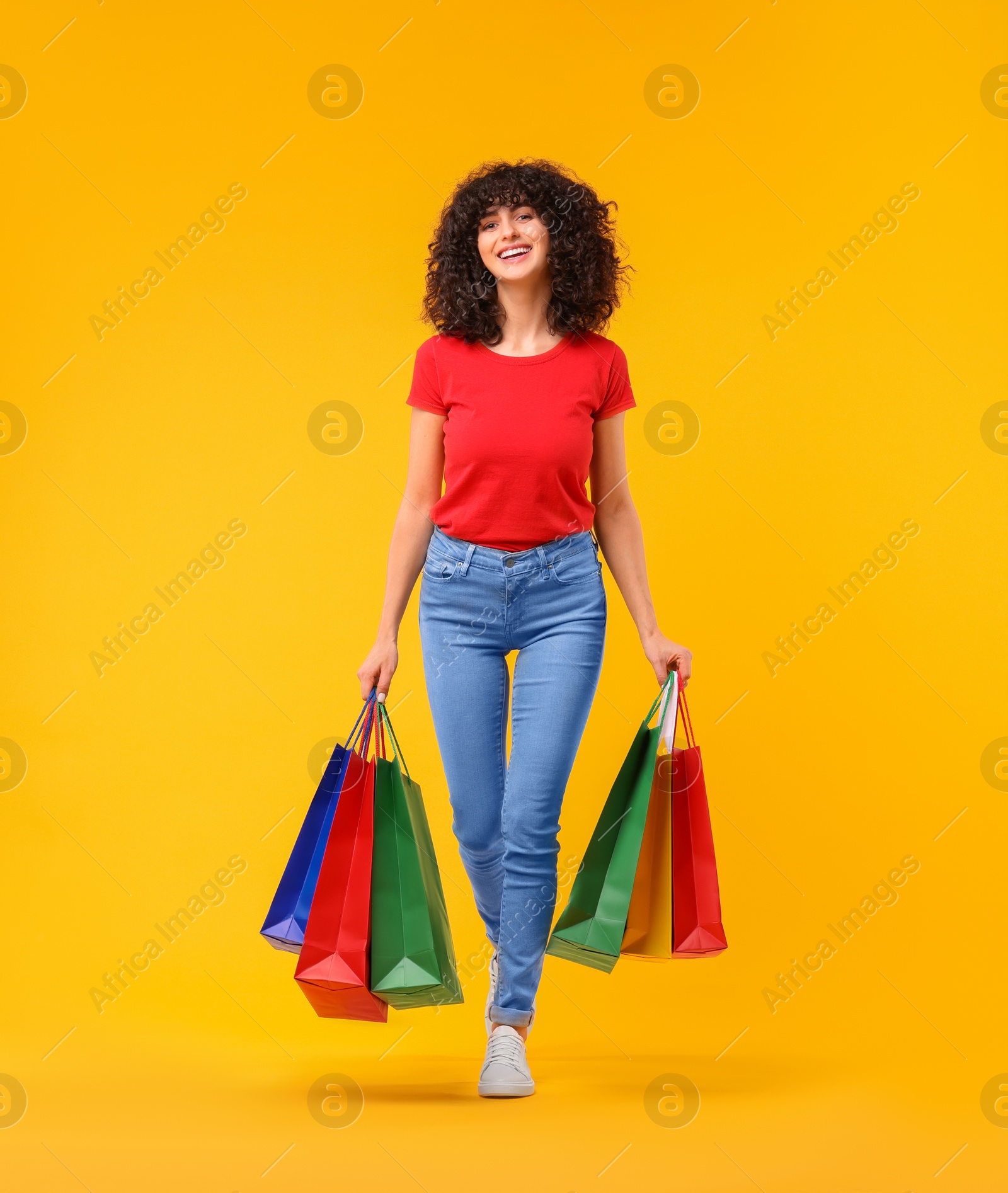 Photo of Happy young woman with shopping bags on yellow background