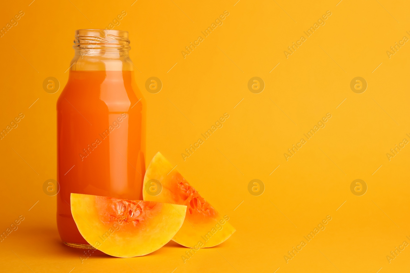 Photo of Tasty pumpkin juice in glass bottle and cut pumpkin on orange background. Space for text