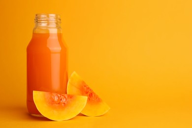 Photo of Tasty pumpkin juice in glass bottle and cut pumpkin on orange background. Space for text