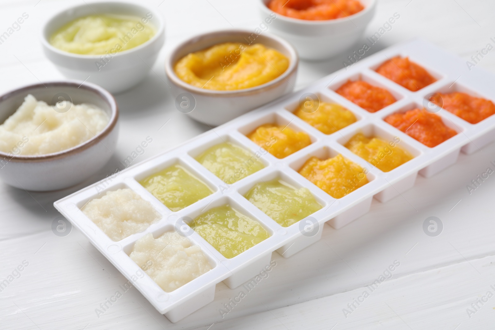 Photo of Different purees in ice cube tray and bowls on white wooden table. Ready for freezing