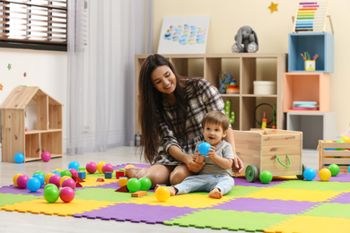 Young nanny and cute little baby playing with toys at home