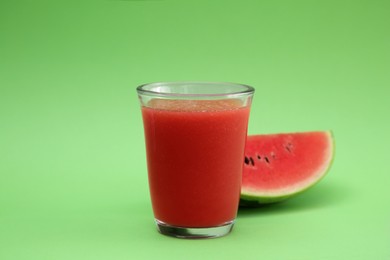 Glass of delicious drink and cut fresh watermelon on light green background