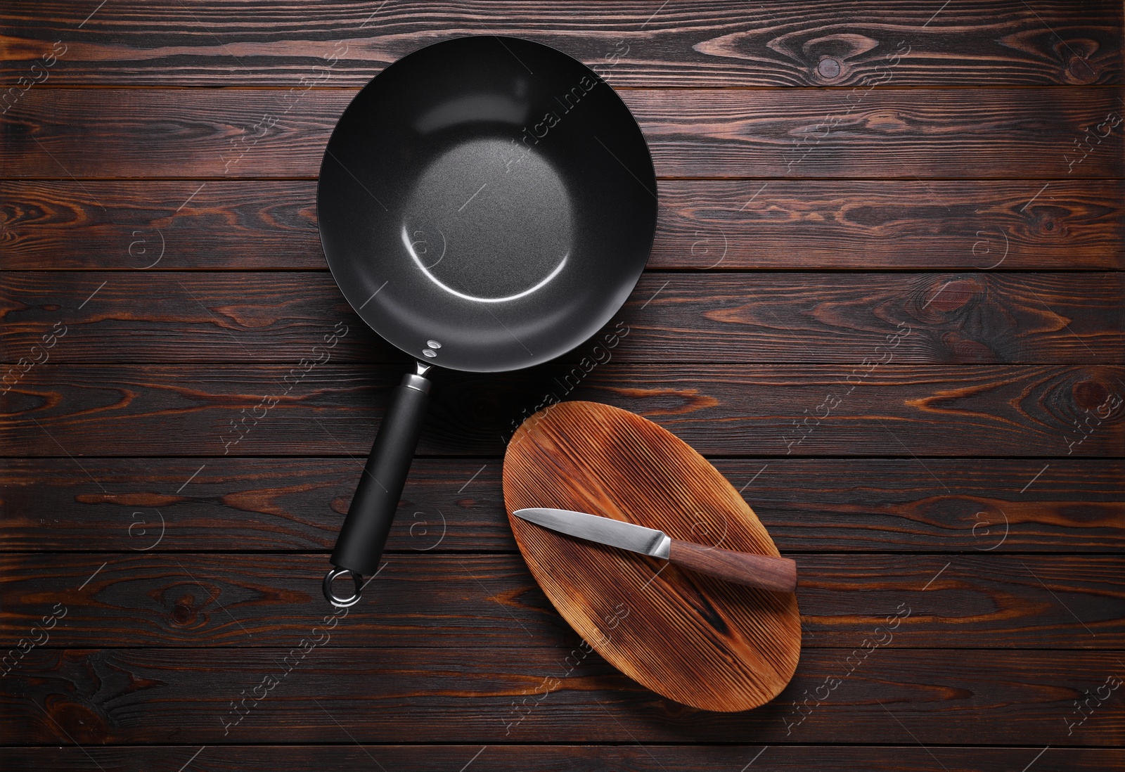 Photo of Empty iron wok, knife and cutting board on wooden table, flat lay