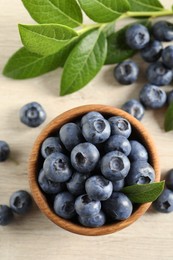 Photo of Bowl of fresh tasty blueberries with leaves on table, flat lay