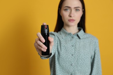 Young woman using pepper spray on yellow background