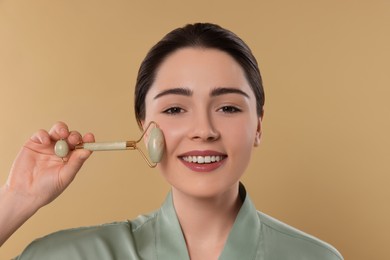 Young woman massaging her face with jade roller on beige background