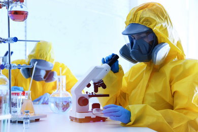 Photo of Scientist in chemical protective suit using microscope at laboratory. Virus research