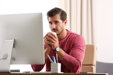 Handsome young man working with computer at table in office