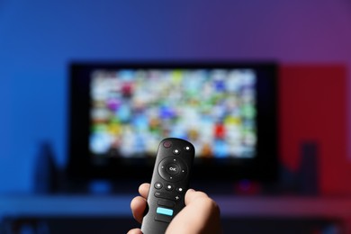 Woman switching channels on TV set with remote control at home, closeup