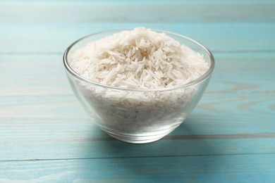 Photo of Raw basmati rice in bowl on light blue wooden table