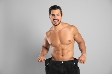 Young man with slim body in old big size jeans on grey background