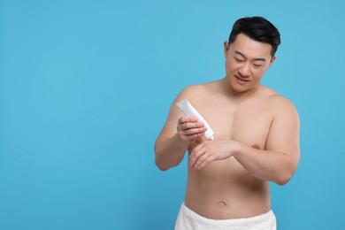 Photo of Handsome man applying body cream onto his hand on light blue background. Space for text